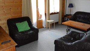 Un espacio acogedor con dos sofás de cuero negro, una mesa de centro de madera y un taburete pequeño. Hay una lámpara sobre una mesita auxiliar y un cuadro en la pared.