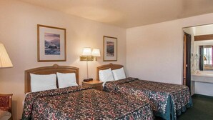 A hotel room with two beds, a bedside table with a lamp, and framed pictures on the wall. - Ashland Valley Inn (Ashland)