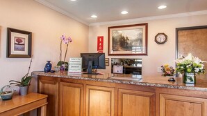 A hotel reception area with a wooden counter, framed artwork, a clock, and a sign indicating continental breakfast. - Ashland Valley Inn (Ashland)