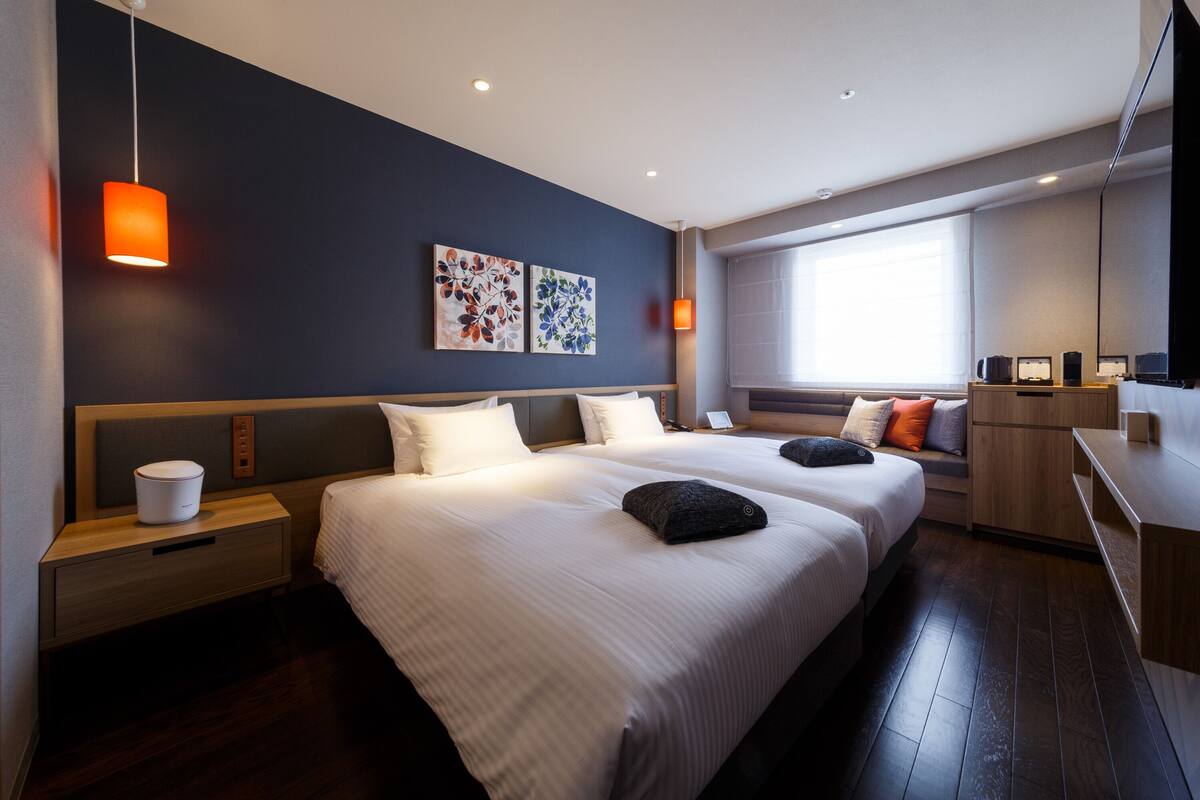 A modern hotel room with two beds, a desk, and a seating area.