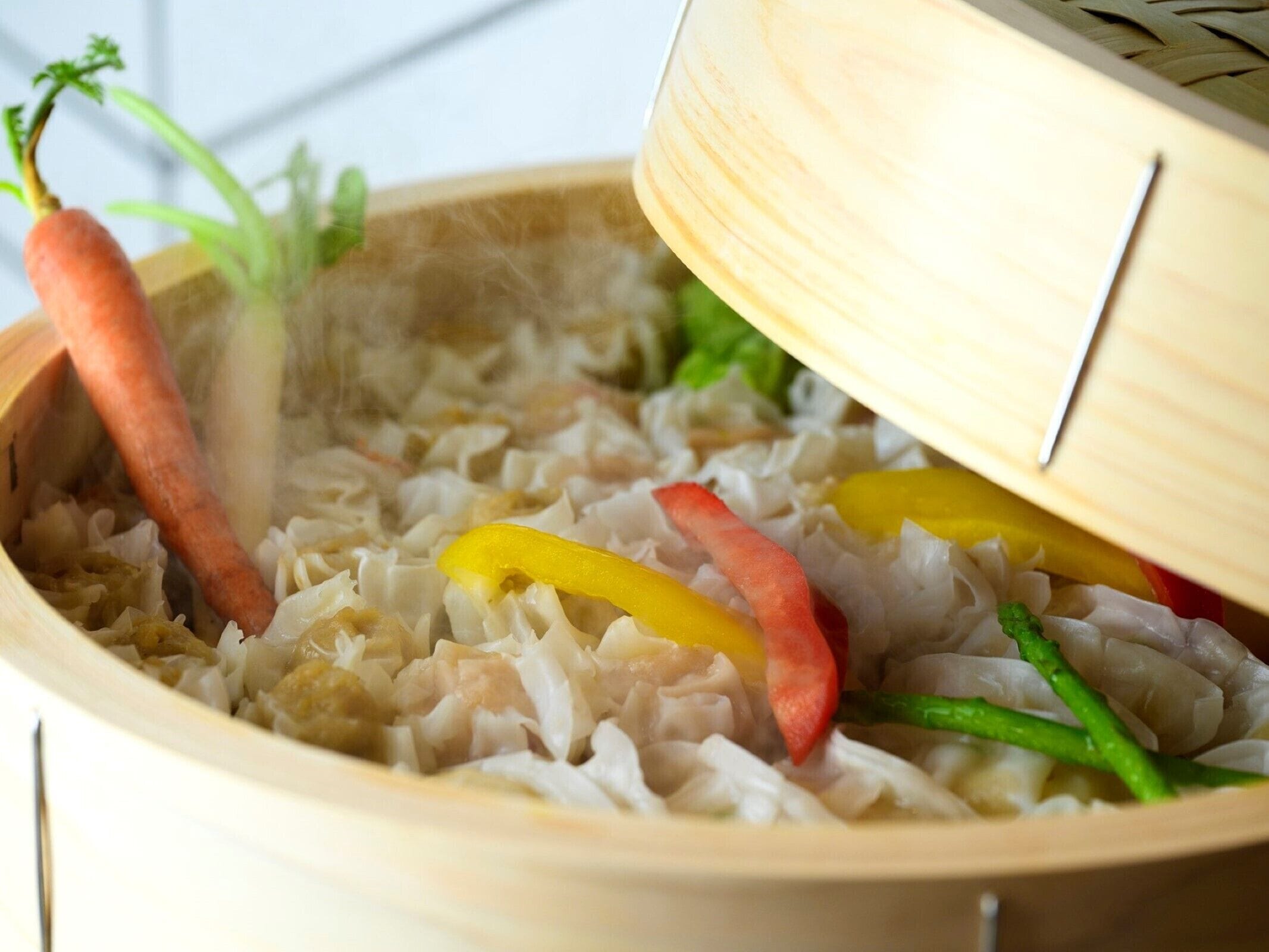 A wooden steamer with vegetables and a lid.