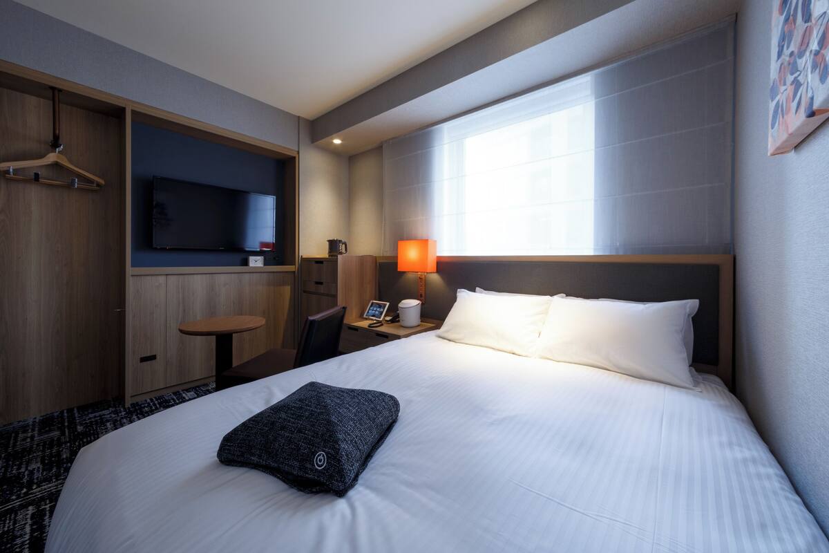 A hotel room with a bed, a desk, a chair, a TV, and a window.