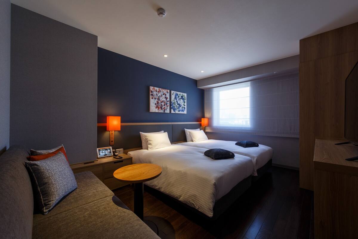 A hotel room with two beds, a sofa, a small table, and artwork on the wall.