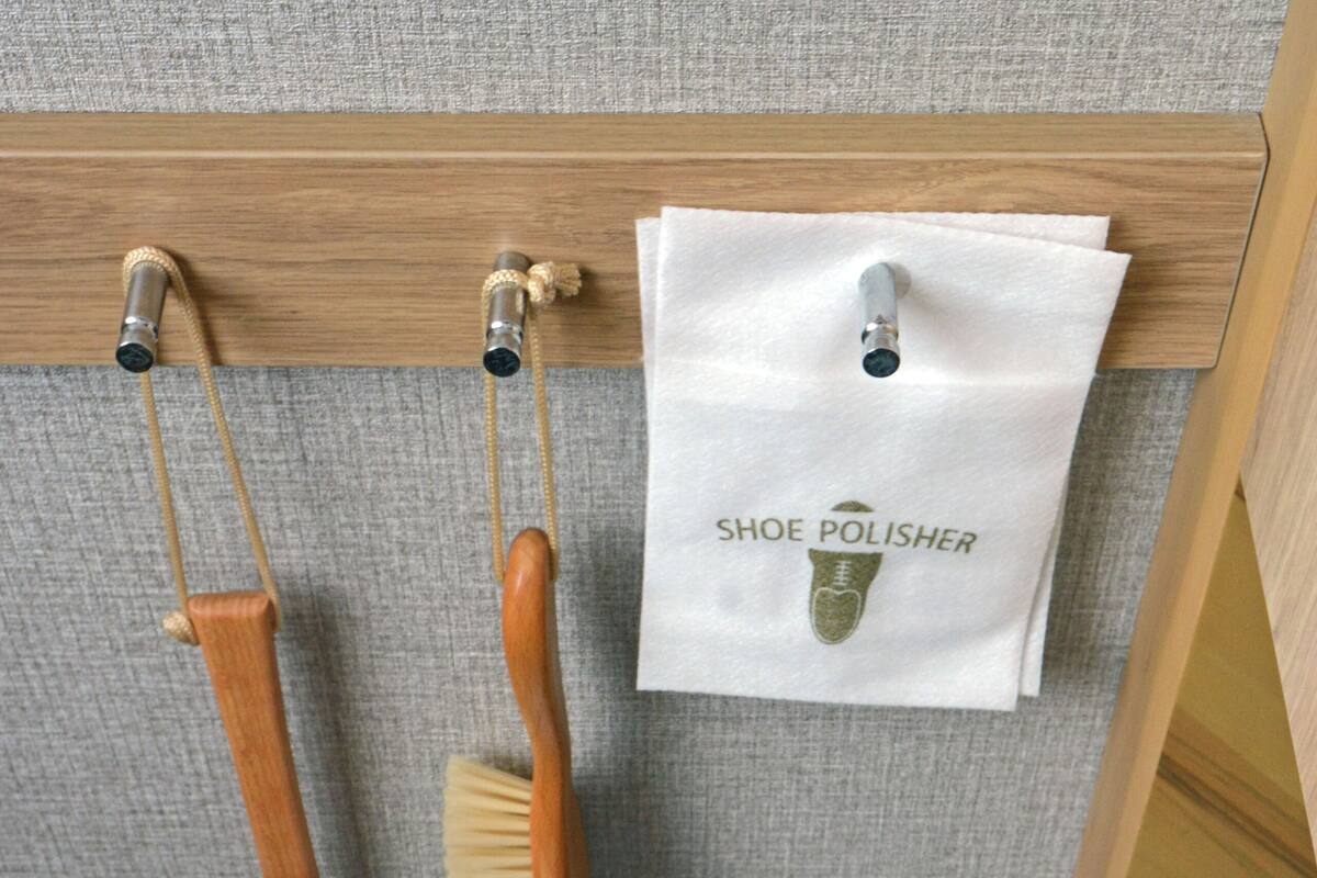 A bathroom with a towel rack holding a wooden brush and a white bag labeled "SHOE POLISHER".