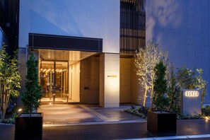 Una entrada de hotel moderna con puerta de cristal, un letrero que dice "FORZA" y un sendero bien iluminado que lleva a la entrada.