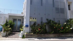 Un edificio moderno con fachada metálica, un buzón azul y plantas en macetas al frente.