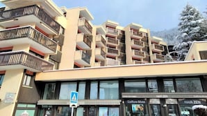 Un edificio a più piani con balconi, una vetrina con insegna e un albero innevato sullo sfondo.
