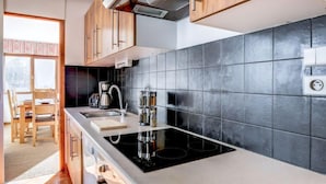 Una cucina moderna con mobili in legno, zoccolo posteriore in piastrelle nere e piano cottura integrato.