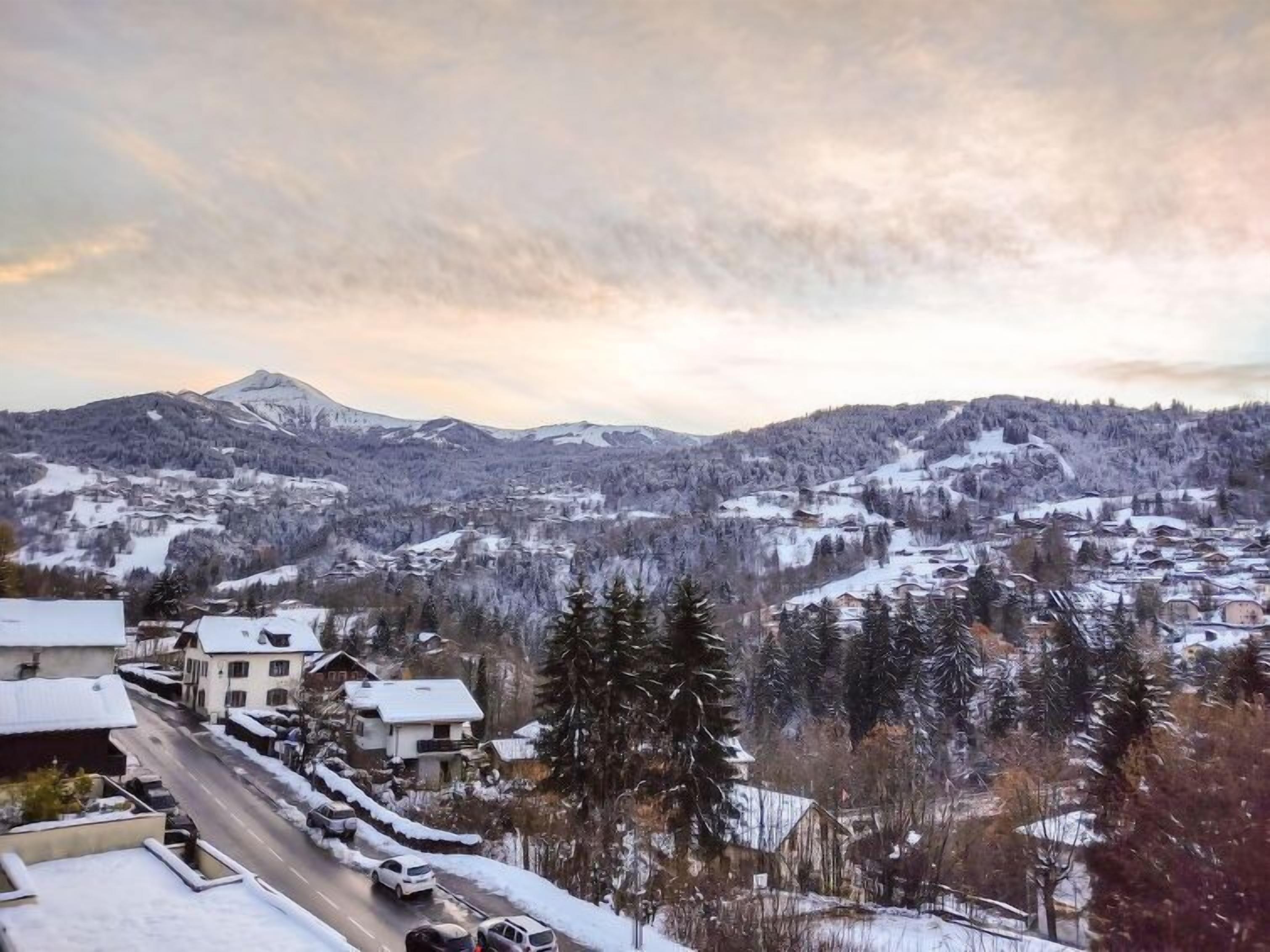 Un pueblo nevado en la montaña con edificios residenciales, una carretera y una montaña al fondo.