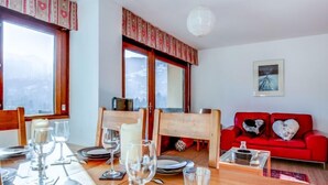 Un'area pranzo con un tavolo di legno apparecchiato per quattro persone, un divano rosso con cuscini a forma di cuore e un'ampia finestra vista su un paesaggio innevato.