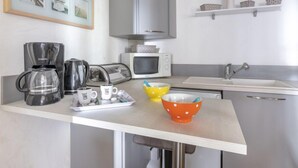 A modern kitchen with a coffee maker, microwave, and a sink. There are framed pictures on the wall and a shelf with baskets. - Bleu Bassin by Interhome (Arcachon)