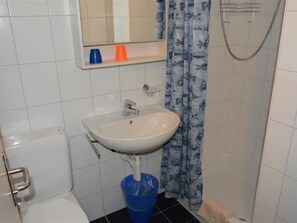 Ein Badezimmer mit einem weißen Waschbecken, einem Spiegel darüber, einem blauen Eimer und einem Duschvorhang mit Fischmuster.