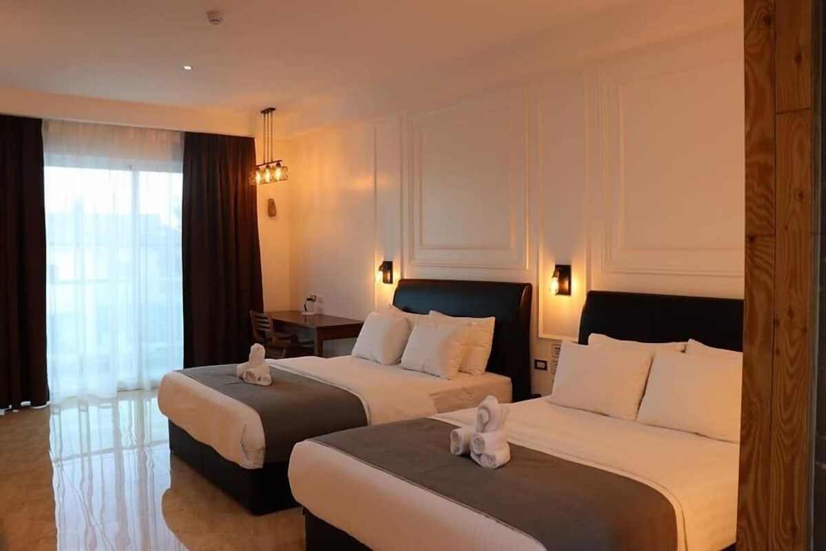 A hotel room with two beds, a desk, and a large window with curtains.