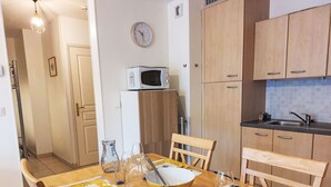 A dining area with a wooden table set for four, a microwave above the cabinets, and a clock on the wall.