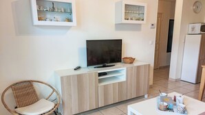 A modern living room with a TV, wicker chair, white cabinet, and a small table with cups.