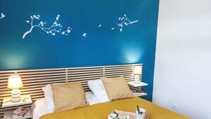 A hotel room with a blue wall, a wooden headboard, two bedside tables with lamps, a bed with a yellow bedspread, and a tray with glasses and a cup.