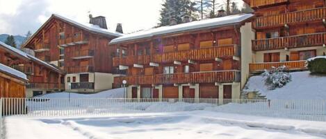 A row of wooden chalet-style buildings with balconies, surrounded by snow.