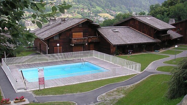 Un edificio in legno rustico con piscina, circondato da un recinto bianco e una strada tortuosa.