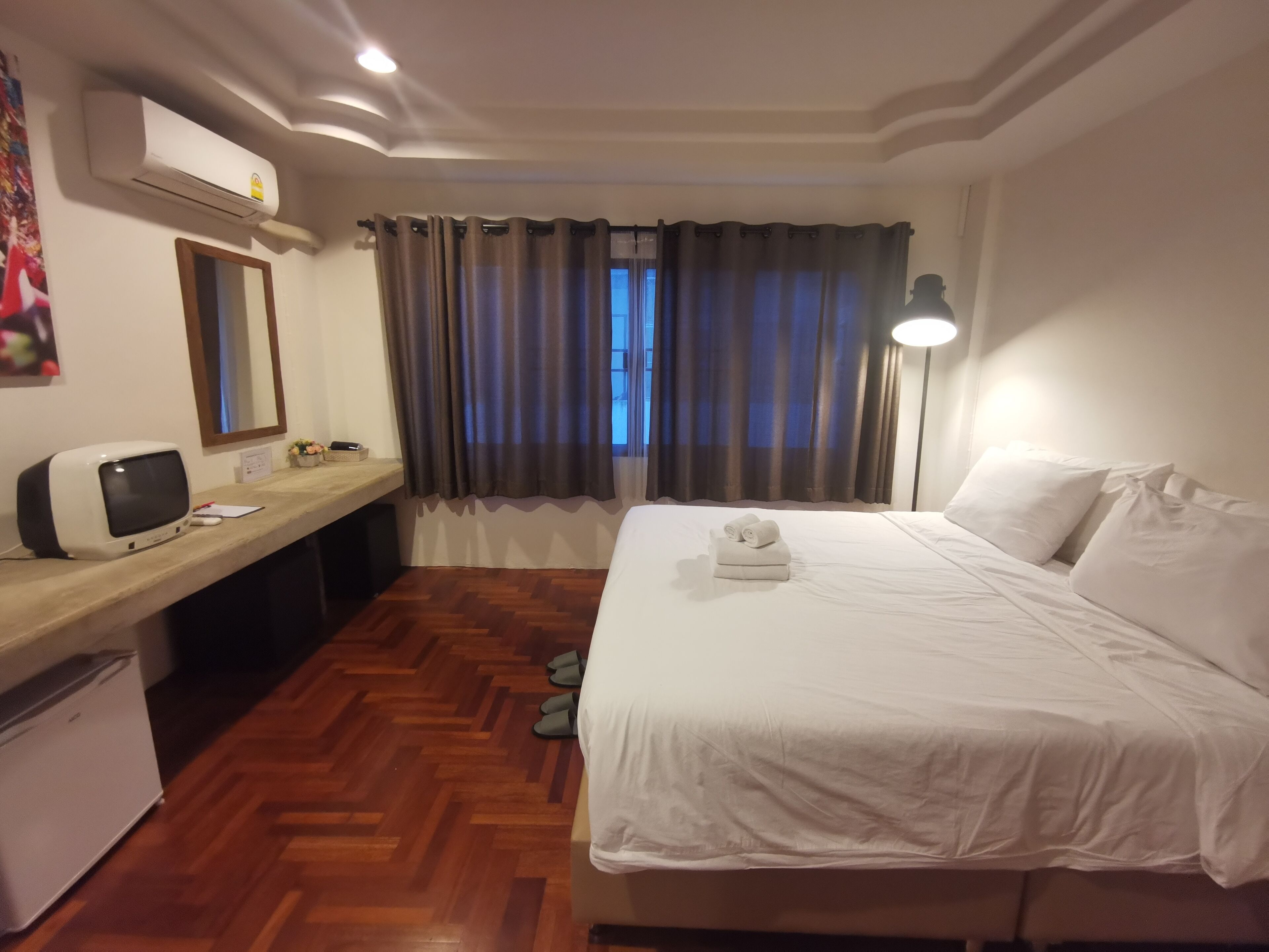 Habitación de hotel con cama, escritorio con ordenador, aire acondicionado y ventana con cortinas.