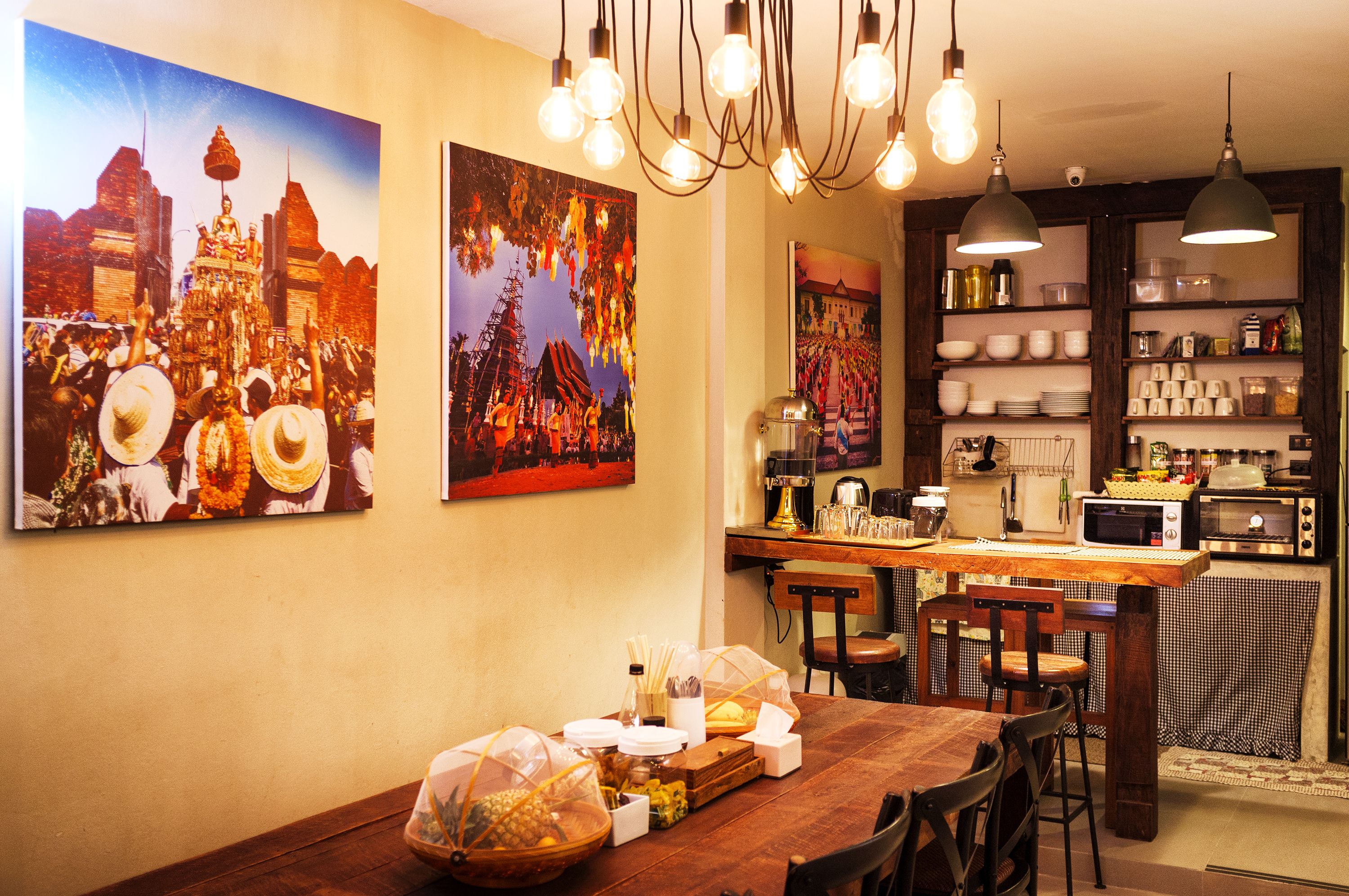 A dining area with a wooden table set for a meal, a kitchen with modern appliances, and wall art depicting cultural scenes.