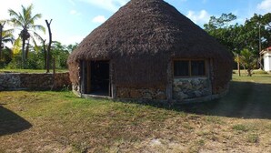 A thatched-roof hut with a stone base, a door, and a window. - Fenepaza (Lifou)
