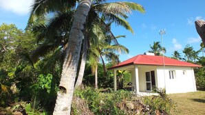 A small white building with a red roof, surrounded by lush greenery and palm trees. - Fenepaza (Lifou)