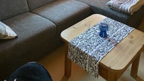 A cozy room with a grey sofa, two windows, and a small wooden table with a patterned tablecloth. - Alphütte Bielerhüs by Interhome (Fiesch)