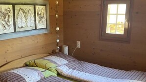 A wooden cabin room with two beds, a window, and a wall-mounted light fixture. - Alphütte Bielerhüs by Interhome (Fiesch)