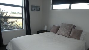 Ein Schlafzimmer mit einem großen Bett, einem Nachttisch, einem Fenster mit Blick ins Freie und einer Wandleuchte.