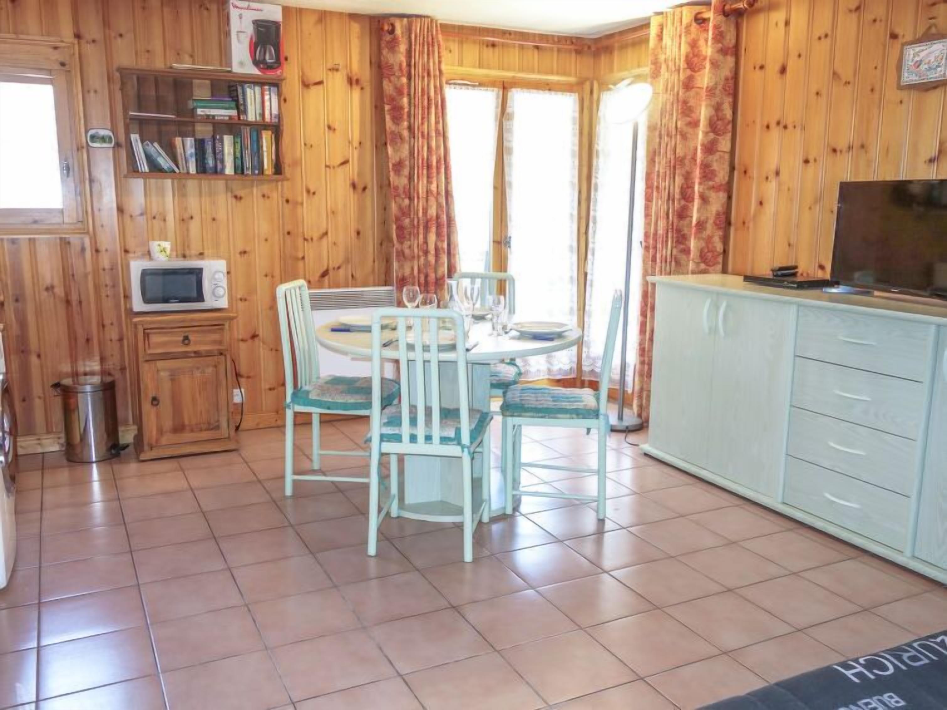 Una habitación acogedora con detalles de madera, una mesa de comedor con sillas, un microondas, un mueble pequeño y un televisor.