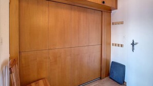 Une pièce comprenant une grande armoire en bois, un petit banc en bois et un tapis bleu sur le sol.