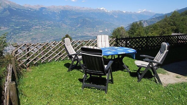 Une terrasse avec deux chaises et une table, d’où l’on peut admirer un paysage montagneux.