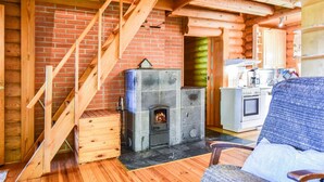Interior de una cabaña de troncos con chimenea, escalera de madera y zona de cocina.