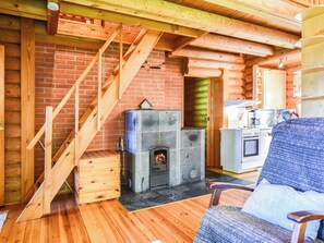 Interior de una cabaña de troncos con chimenea, escalera de madera, zona de cocina y un espacio de estar acogedor.