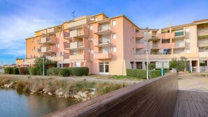 Un edifici residencial de diverses plantes amb balcons, un passeig de fusta i un cos d'aigua al primer terme.