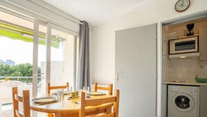 Cuina compacta amb rentadora, microones i zona de menjador amb taula i cadires.