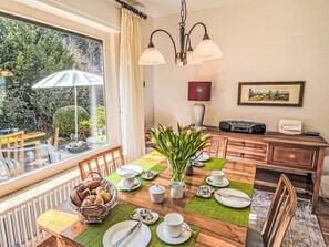 A dining area with a table set for four, a vase of flowers, and a view of the outdoors.