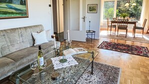 Una sala de estar con un sofá, una mesa de centro con copas de vino, un mantel de encaje y una alfombra estampada.