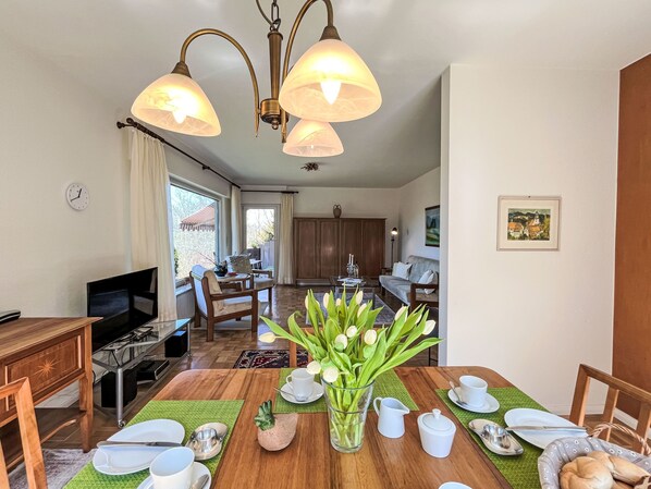 A dining area with a wooden table set for four, a vase of tulips, and a kitchen in the background.