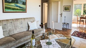 Una sala de estar con un sofá, un cuadro, una botella de vino, copas, un candelabro y una zona de comedor con una mesa y sillas.
