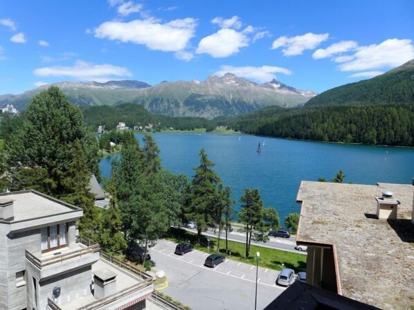 A view of a lake surrounded by mountains, with a parking area and buildings in the foreground.