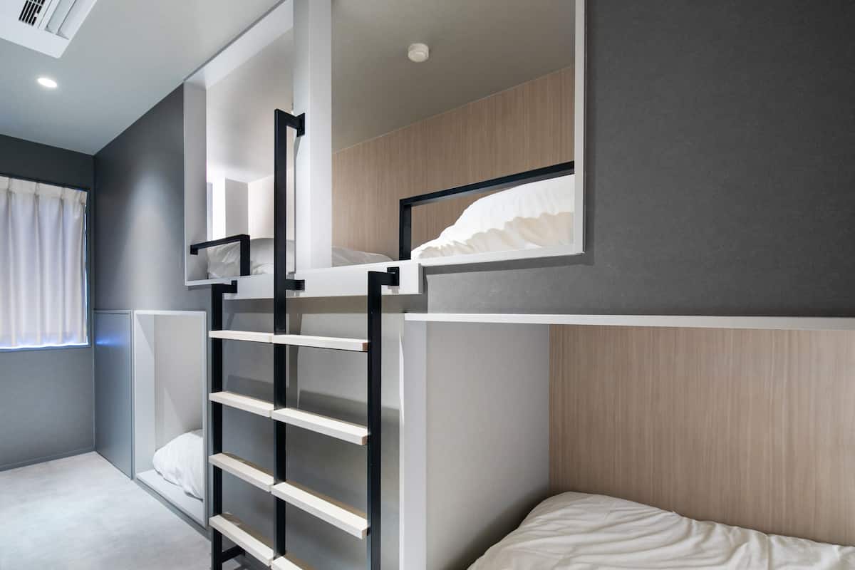 Una cama litera con escalera, una ventana con cortinas y una estantería fijada a la pared.