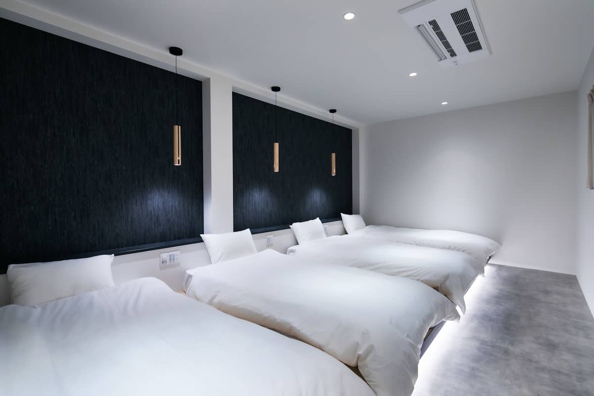 Una habitación de hotel moderna con tres camas, paneles de pared oscuros e iluminación colgante.