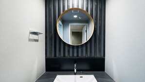 Een moderne badkamer met een rechthoekig wastafel, een ronde spiegel en een wandpaneel van hout.