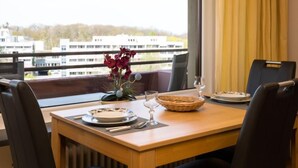 Ein Esszimmertisch ist mit Tellern, Besteck und einer Blumenvase gedeckt, mit Blick auf Gebäude durch ein Fenster.