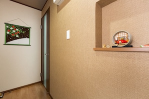 Un couloir avec un mur à texture, un tableau encadré représentant des fleurs, une porte et une étagère sur laquelle est posé un objet décoratif.