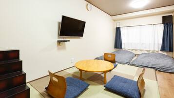 Habitación compacta con cama, televisor en la pared, una mesita y una silla.