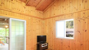 Quarto com paredes e chão de madeira, porta de vidro deslizante, janela e televisão sobre um suporte de madeira.