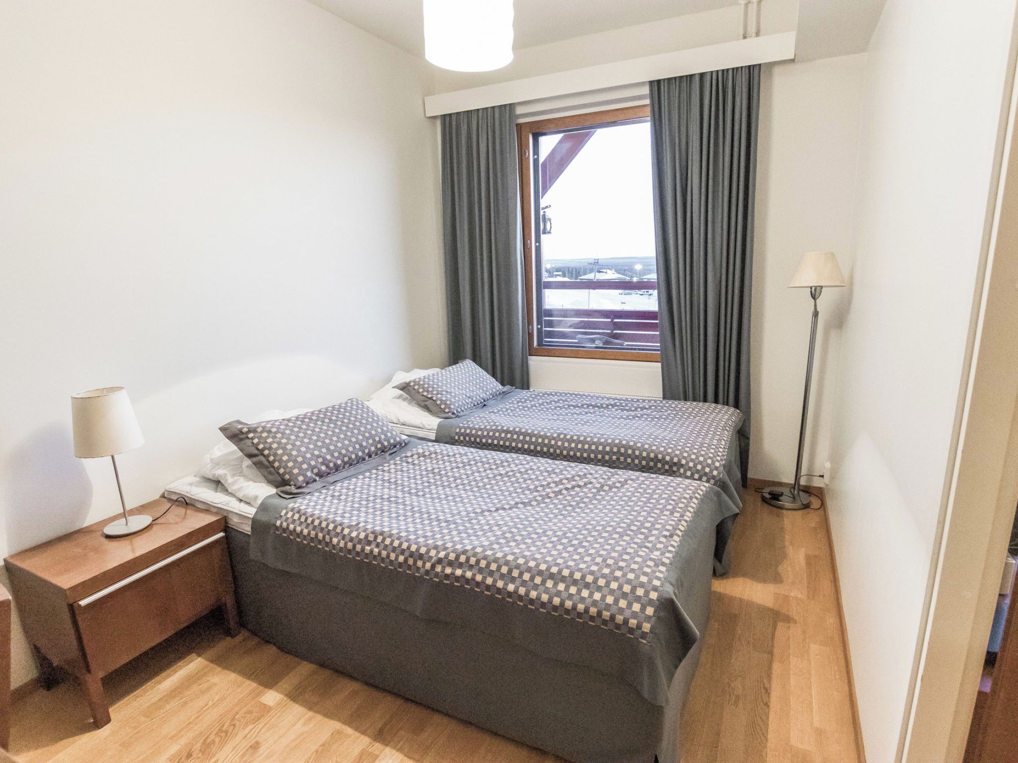 Ein Hotelzimmer mit zwei Betten, einem Nachttisch, einer Lampe und einem Fenster mit Vorhängen.