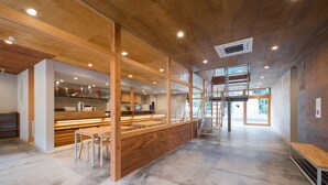 A spacious interior with a wooden ceiling, a central bar area, and a staircase leading to an upper level. - Mt.Takao Base Camp - Hostel (Hachioji)